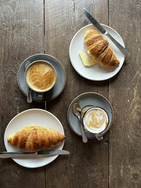Croissant with butter and cups of coffee on a rustic wooden table