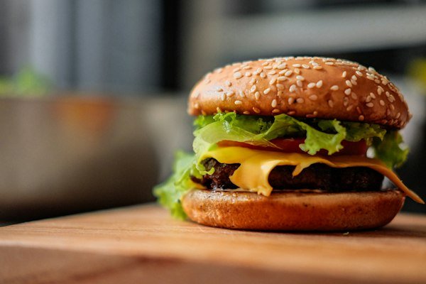 A cheeseburger layered with lettuce and tomato on a wooden board