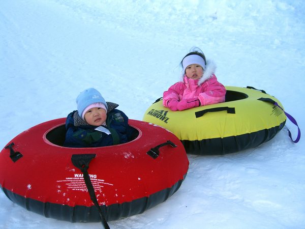Two children sitting in colorful snow tubes